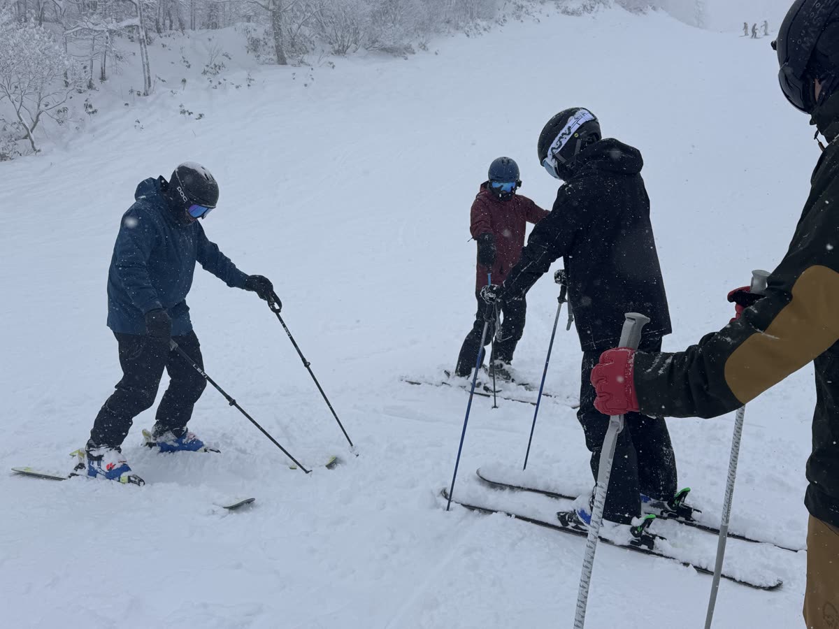 教練在飄雪的雪道上示範雙板動作,學員在旁觀察