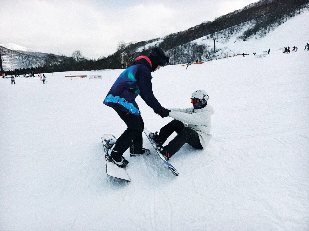 教練伸手把跌坐在雪地上的單板學員拉起來